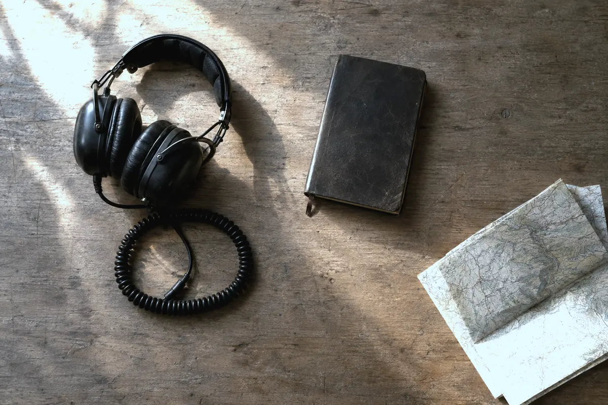 An aviation headset, a logbook and a folded chart on a worn wooden desk