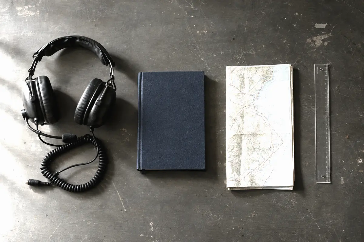 An aviation headset, logbook, chart and plotter laid out on a workbench