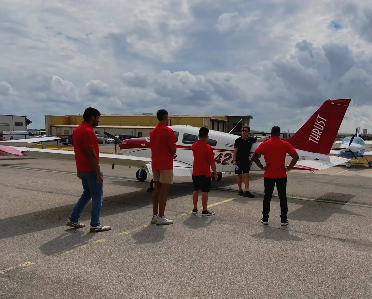 A Thrust Flight instructor briefing four students beside a Piper Archer on the ramp