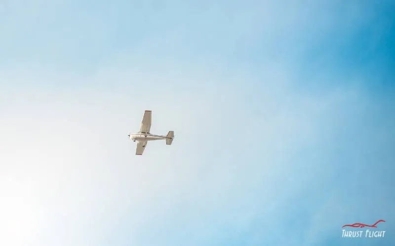 Small training airplane high overhead against a pale sky